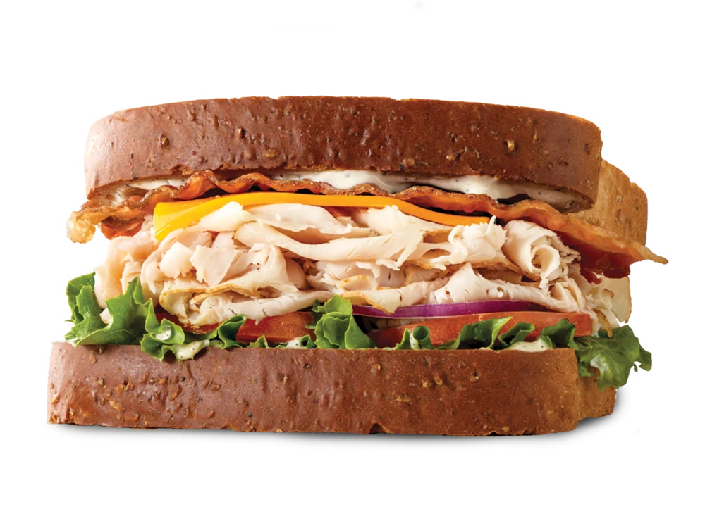 Arby's Roast Turkey Ranch & Bacon Sandwich with turkey, bacon, cheddar cheese, lettuce, tomato, red onion, and ranch sauce on honey wheat bread.